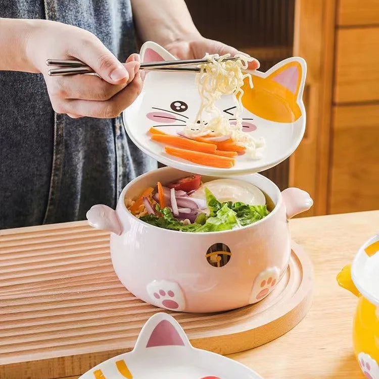 Person using a cat-shaped kawaii ramen bowl to eat noodles with vegetables on a wooden table.