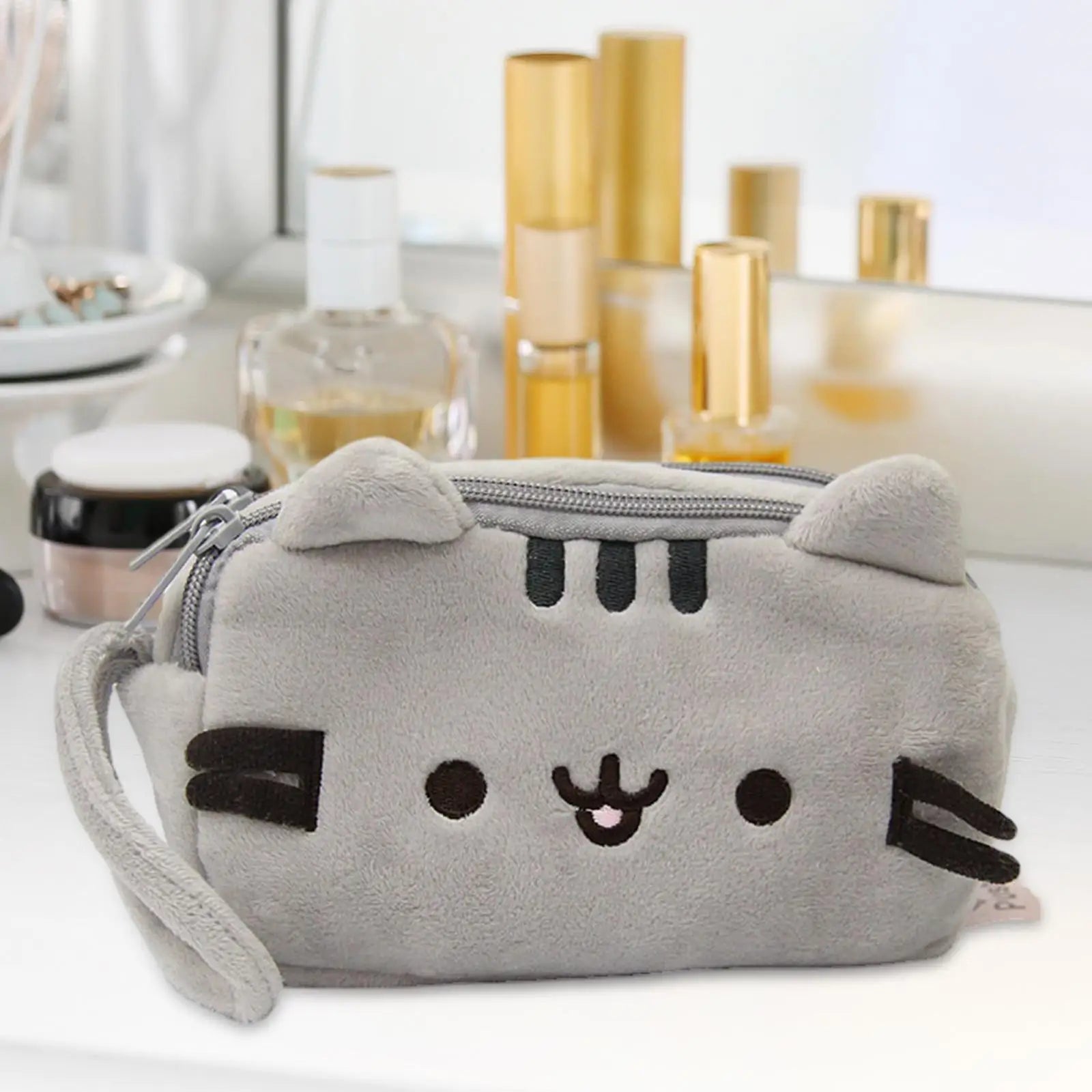 Gray cat-shaped kawaii pouch with a zipper on a blurred background of cosmetic products.