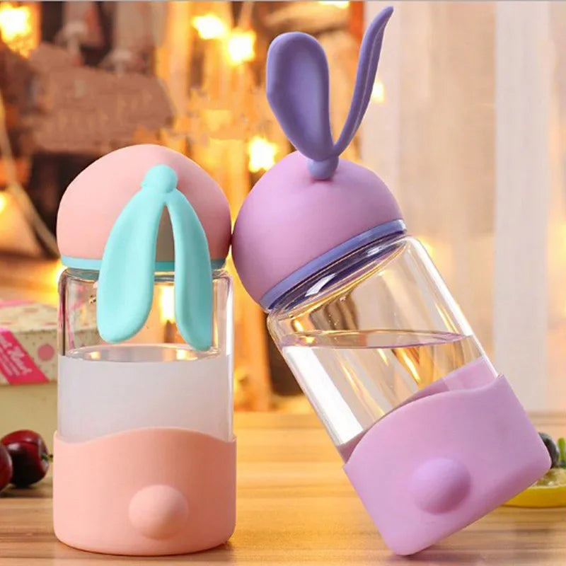 Two colorful kawaii water bottles with bunny ears on a wooden surface.