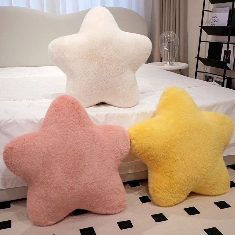 Three star-shaped cushions in white, pink, and yellow on a bed.