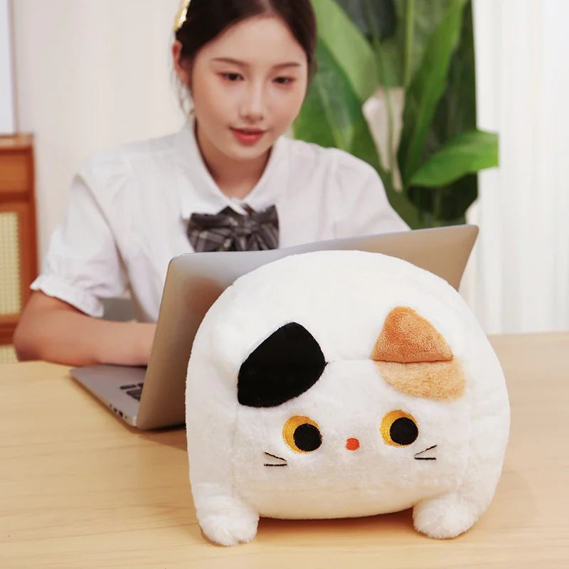 Person using a laptop with a kawaii plush toy resembling a cat face on a desk.