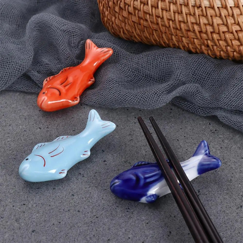 Three fish-shaped ceramic kawaii chopstick rests on a gray surface with a woven basket in the background.