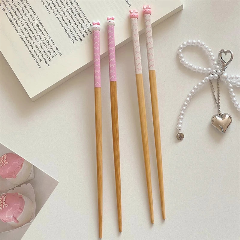 Three wooden kawaii chopsticks with pink accents on a light surface, next to a heart-shaped pendant.