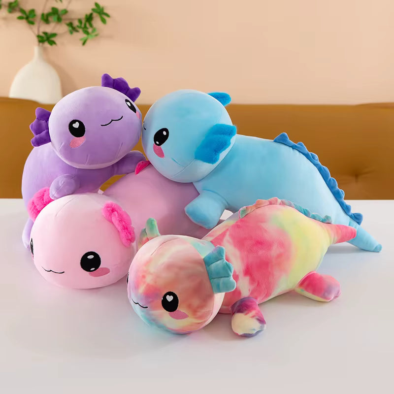 Four cute plush axolotl toys in different colors and tie-dye patterns, arranged together on a white table against a soft beige wall background.
