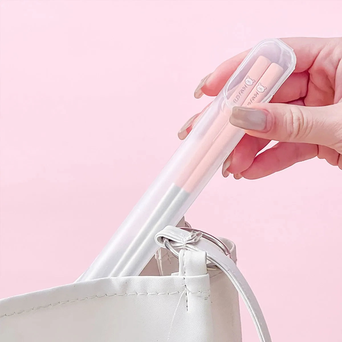 Hand holding a white and pink kawaii chopsticks with a clear case against a pink background