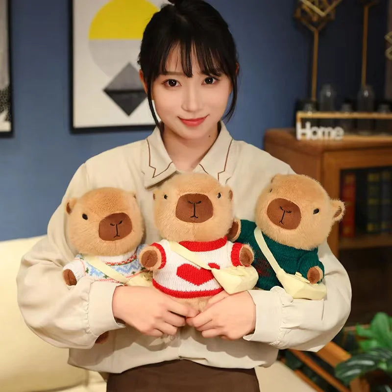Person holding three kawaii teddy bears wearing sweaters in a cozy indoor setting