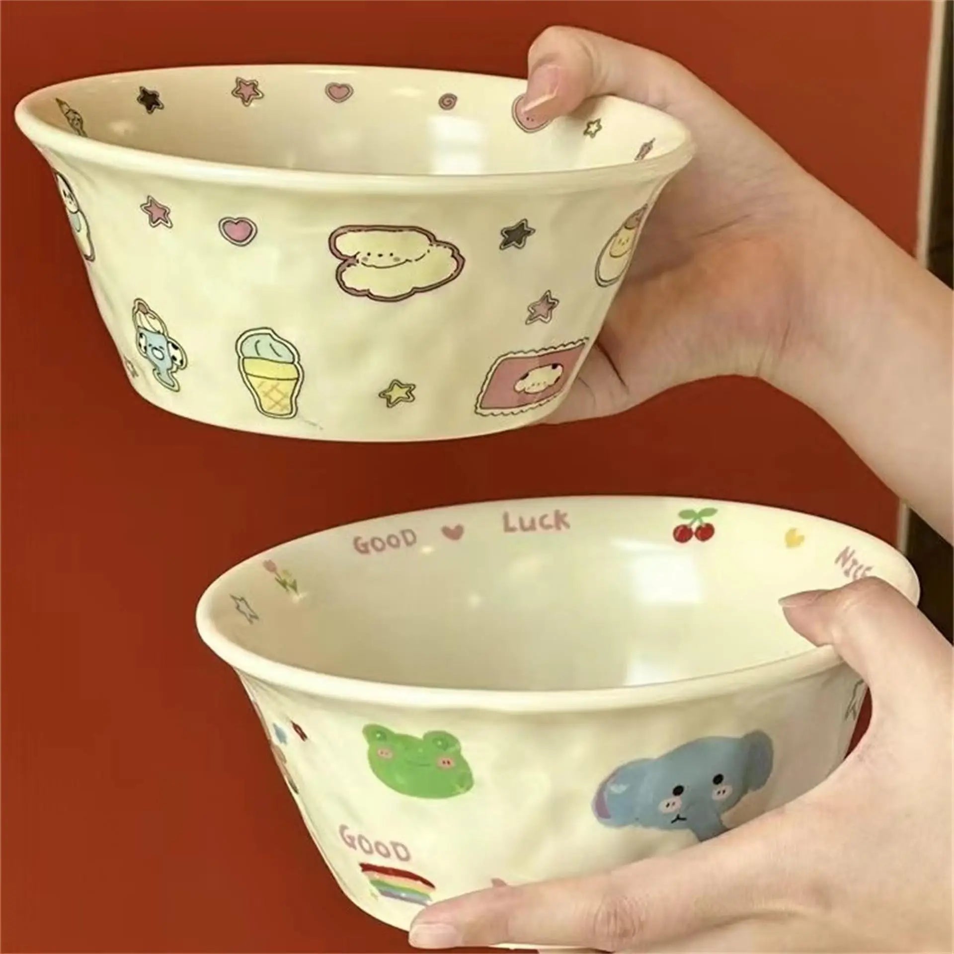Two ceramic kawaii ramen bowls with cute illustrations held by hands against a red background