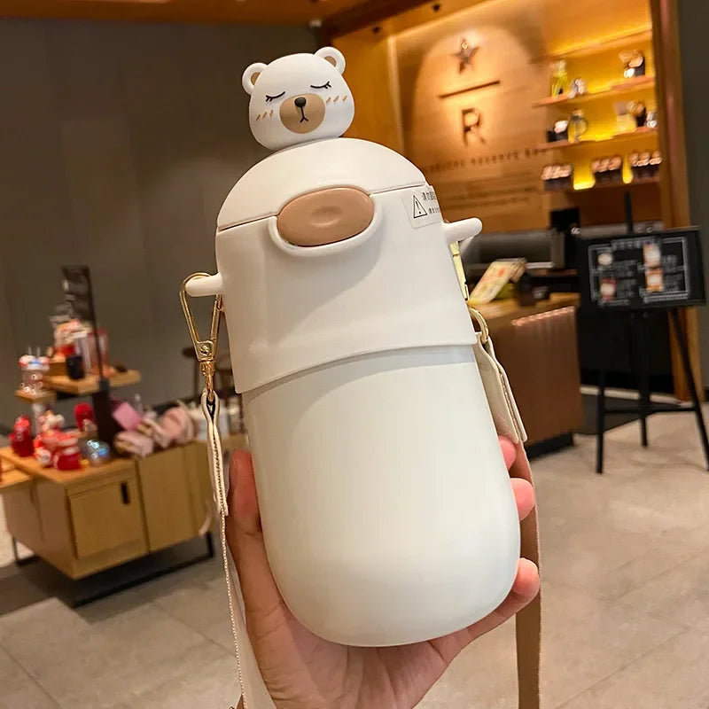 White bear-shaped kawaii water bottle held in a hand with a blurred cafe background
