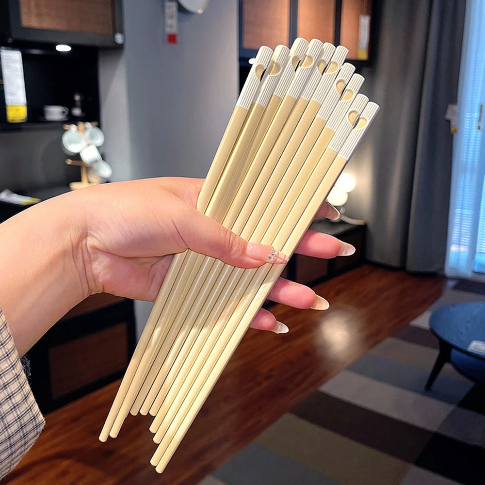 Hand holding a set of wooden kawaii chopsticks with a blurred indoor background