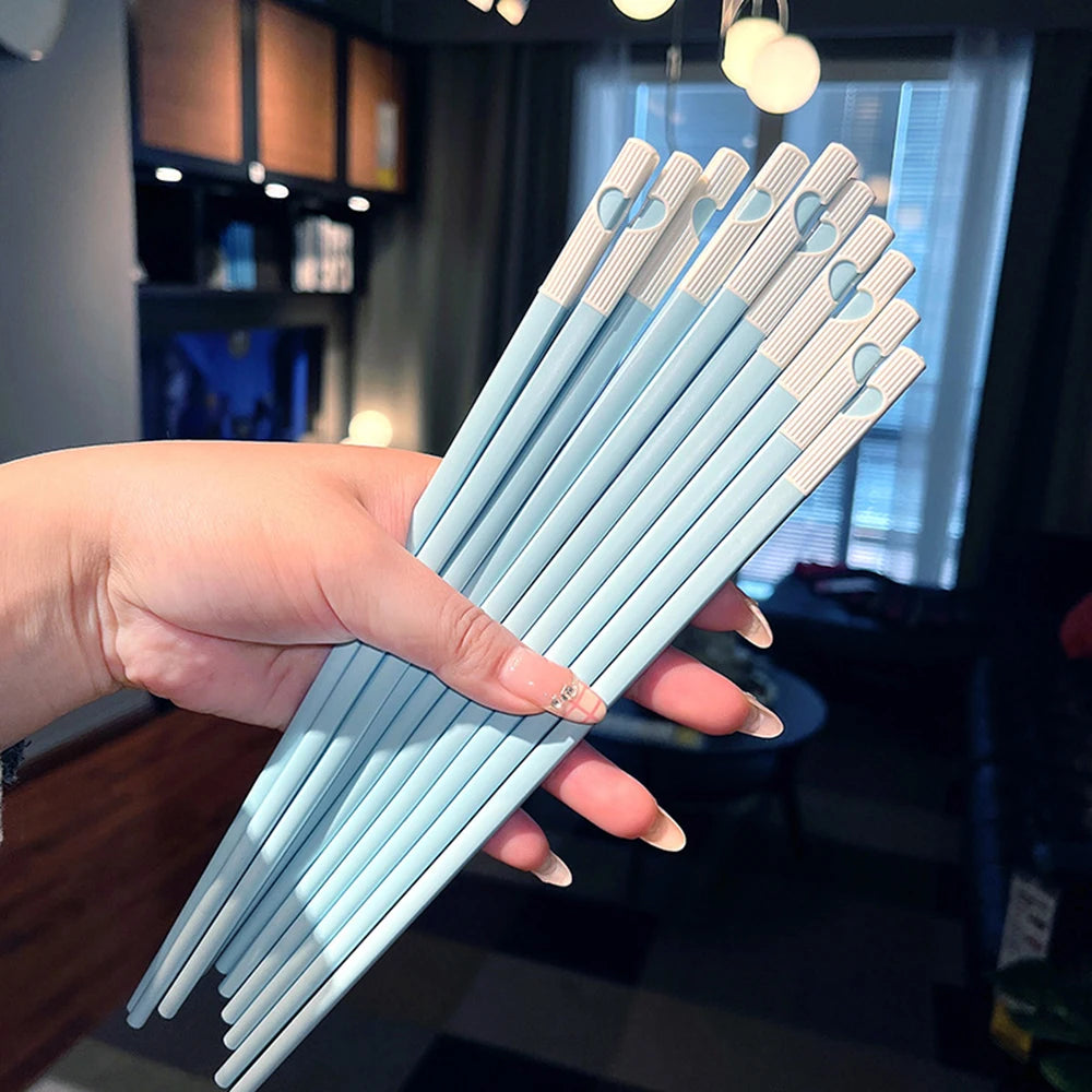 Hand holding a set of light blue and white kawaii chopsticks with heart designs.