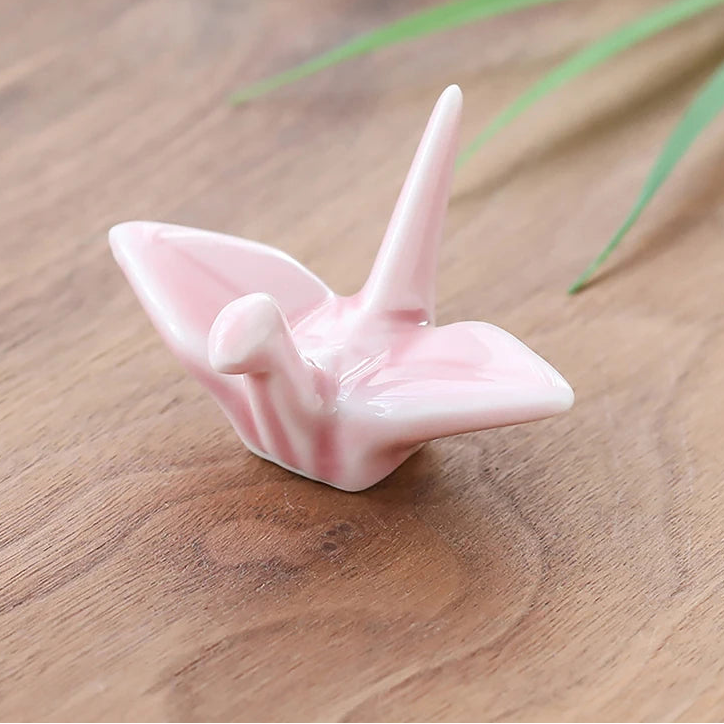 Pink ceramic kawaii chopstick holders on a wooden surface with green leaves in the background