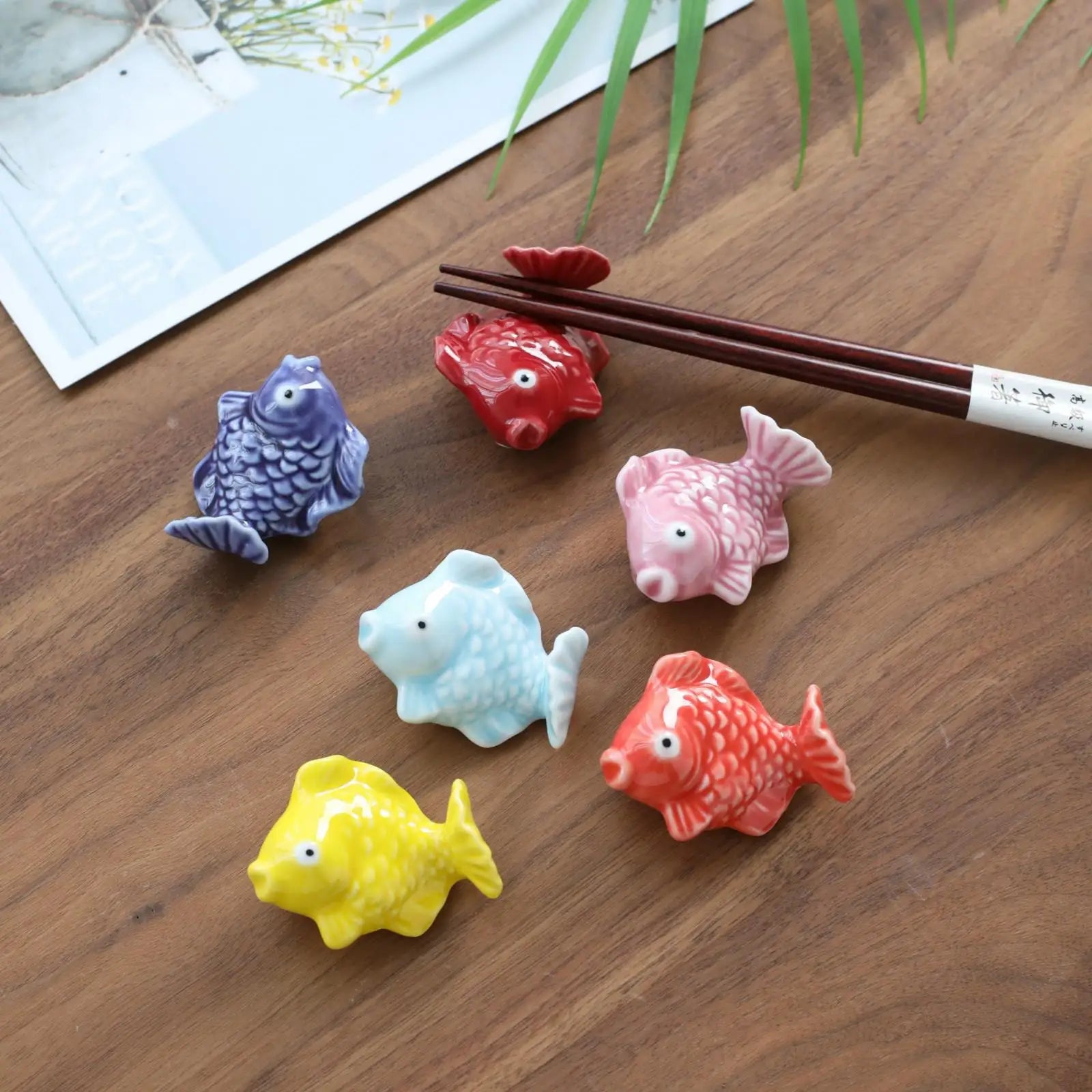 Colorful fish-shaped kawaii ceramic chopstick holders on a wooden surface with chopsticks.