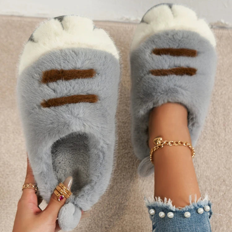 Gray fuzzy slippers with brown accents worn indoors on a carpeted floor.