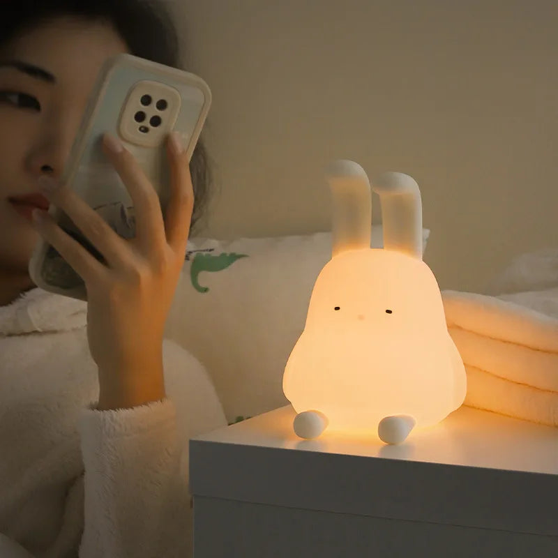 Person using a phone with a glowing rabbit-shaped kawaii night light on a table.