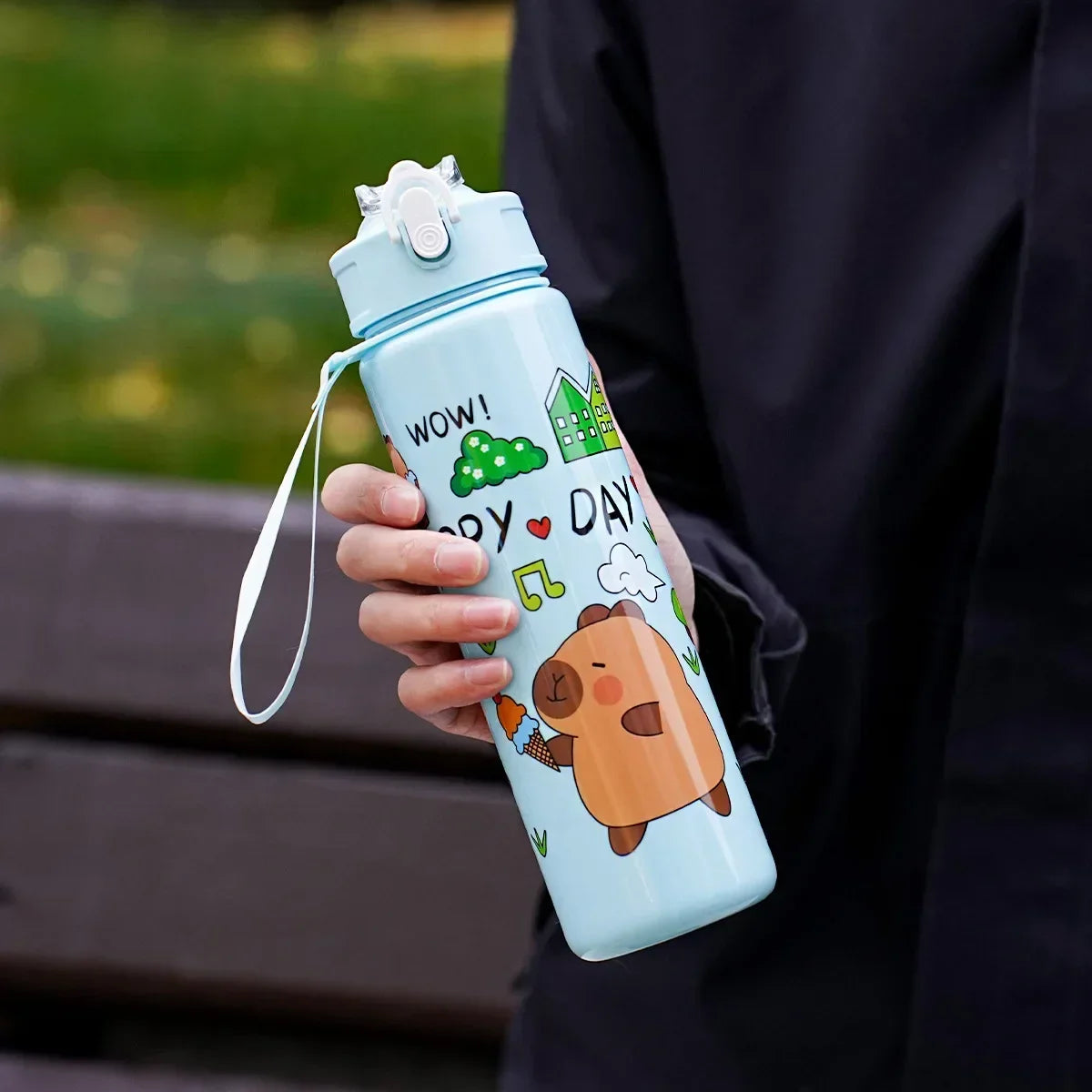 Person holding a cartoon-themed kawaii water bottle with a bear design outdoors.