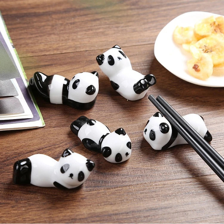 Panda-shaped kawaii chopstick holders on a wooden surface with chopsticks and food in the background.