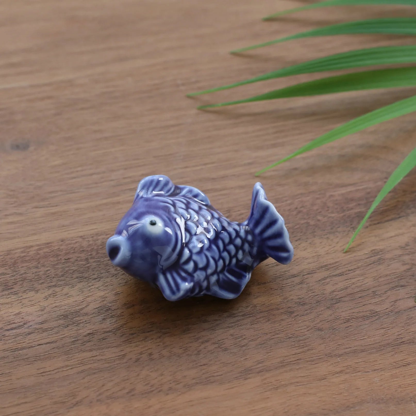 Blue ceramic fish kawaii chopstick holders on a wooden surface with green leaves.