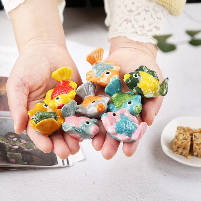 Colorful fish-shaped kawaii chopsticks holders held in hands on a light surface.