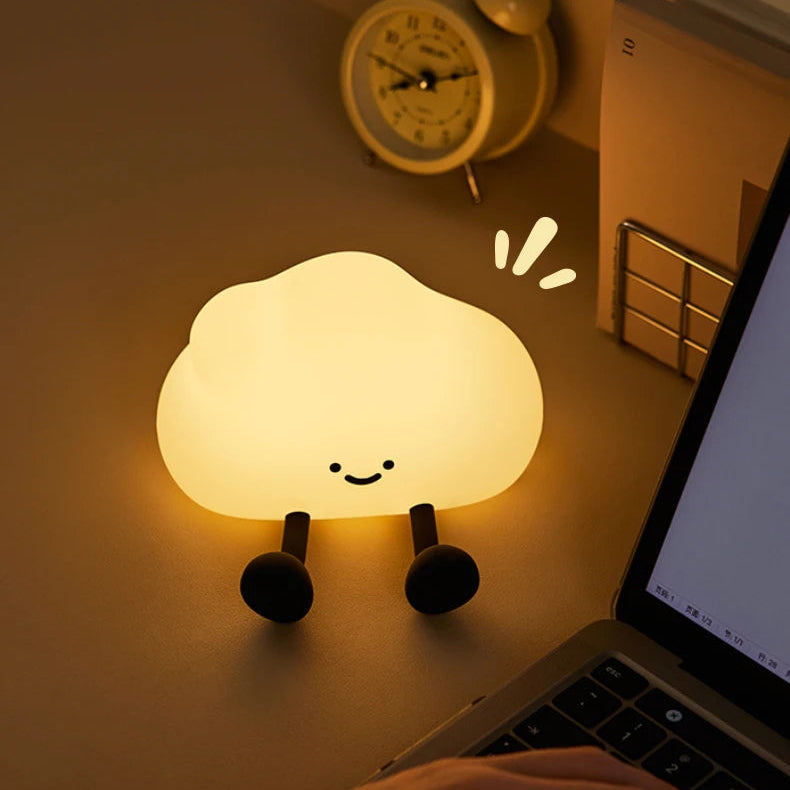 Cloud-shaped kawaii night light on a desk with a laptop and alarm clock in the background.