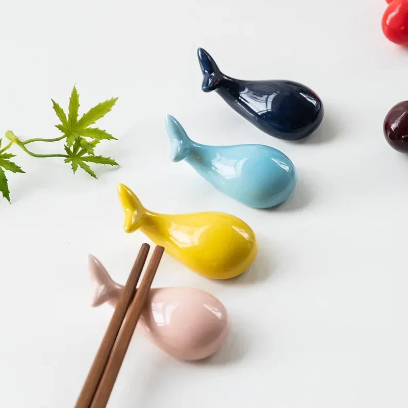 Colorful ceramic whale-shaped kawaii chopstick holders on a white surface with chopsticks.