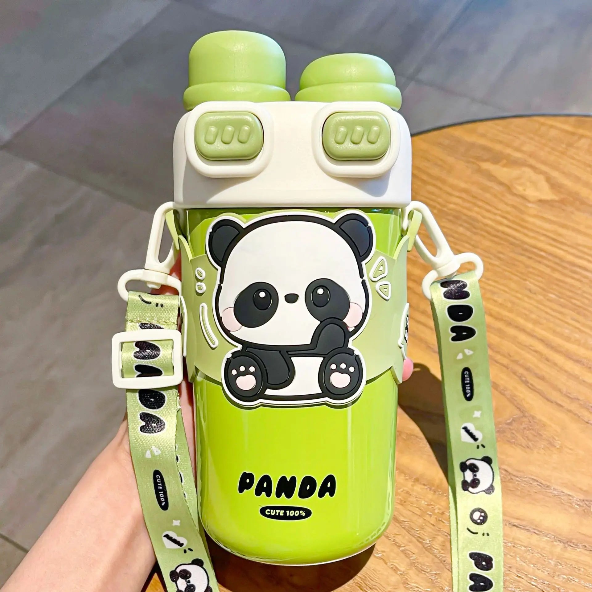Green kawaii water bottle with panda design and strap on a wooden surface