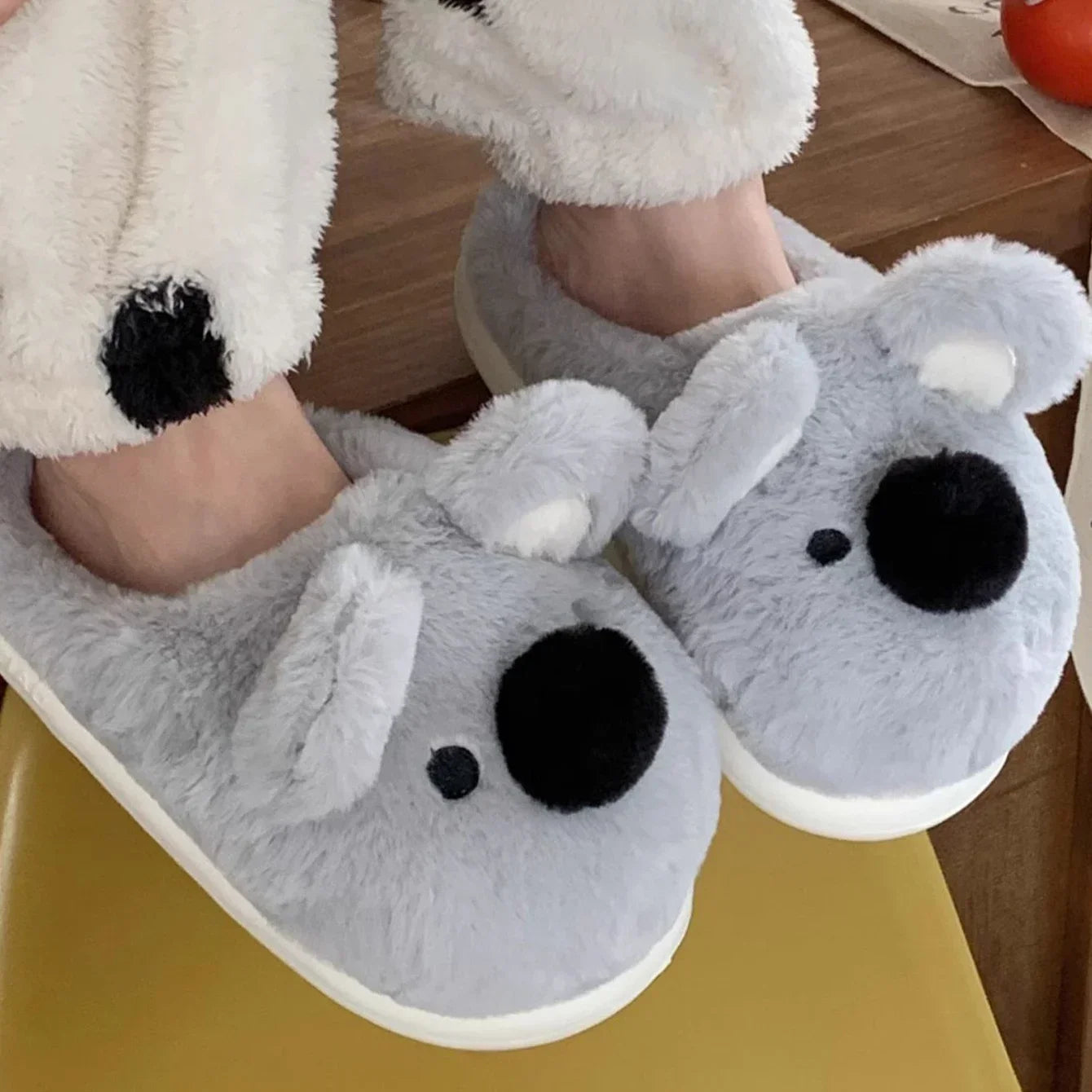 Gray kawaii slippers shaped like koalas worn by a person on a wooden floor.