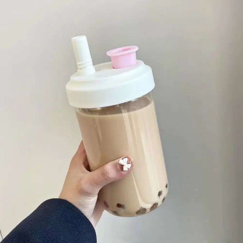 Hand holding a clear bubble tea kawaii cup with a white straw and pink cap against a plain background
