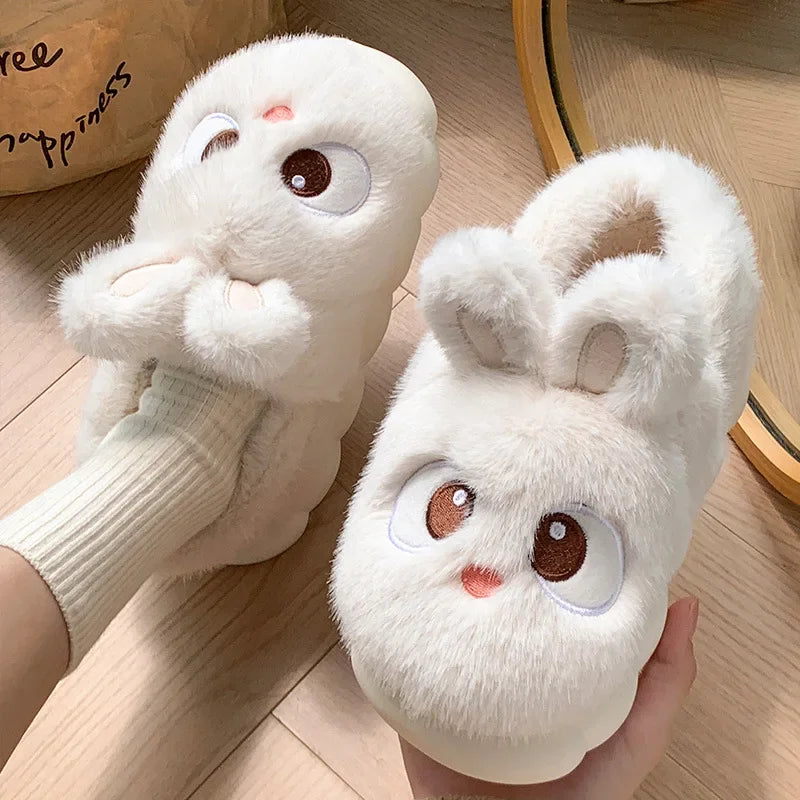 Pair of white bunny kawaii slippers with cartoon face design on a wooden floor.