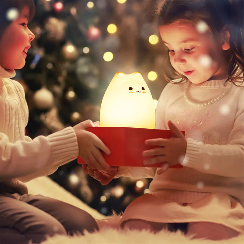 Two children holding a glowing kawaii cat-shaped night light in front of a Christmas tree.
