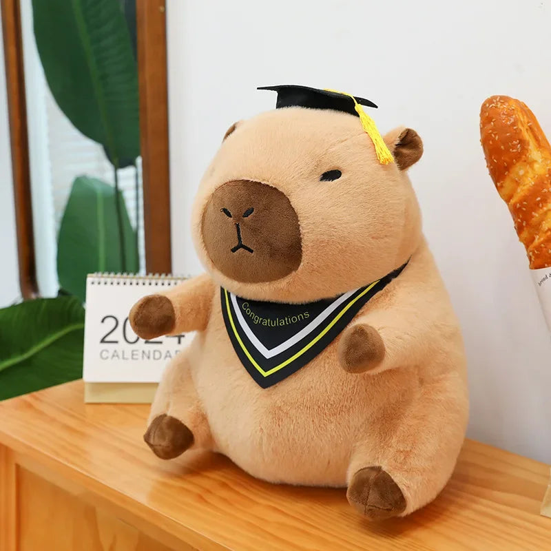 Kawaii plush toy bear with graduation cap and sash on a wooden surface with plants and a calendar in the background.