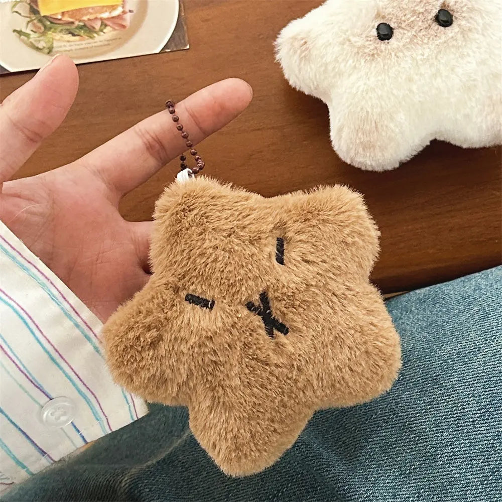 Plush kawaii keychain shaped like a bear held by a hand on a wooden surface with a plush toy in the background.