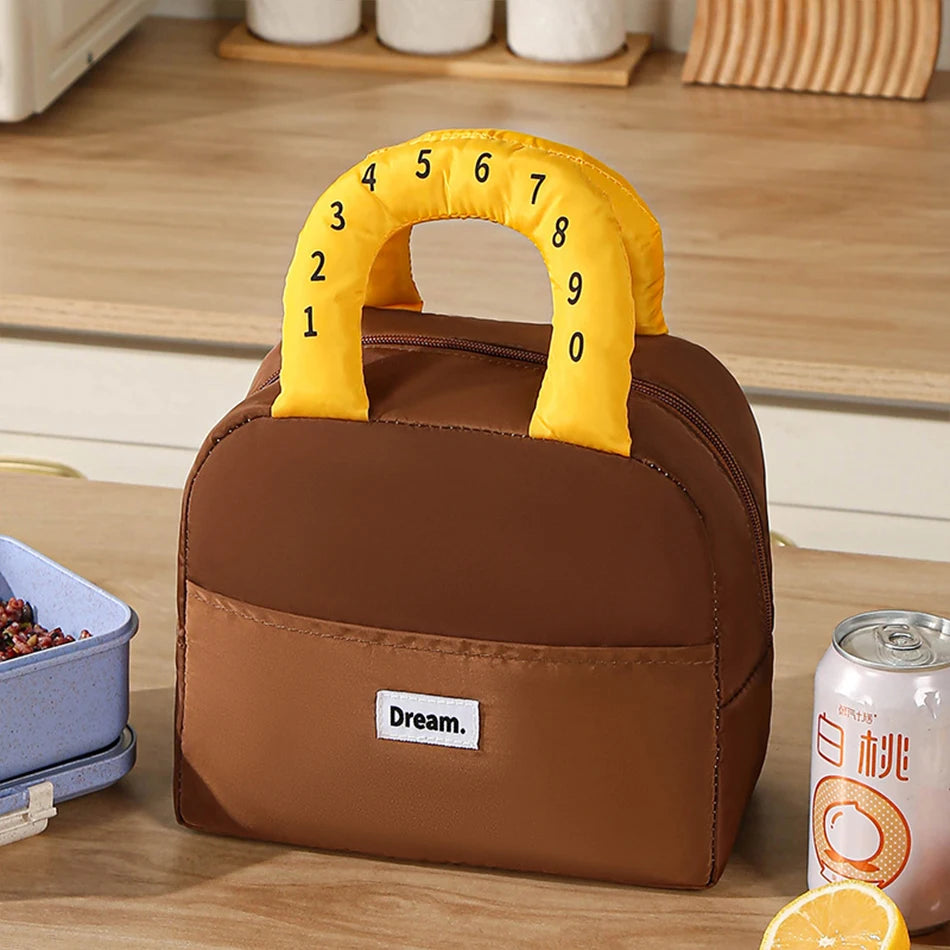 Brown kawaii lunch bag with yellow number handle on a wooden surface, next to a can of drink and container.