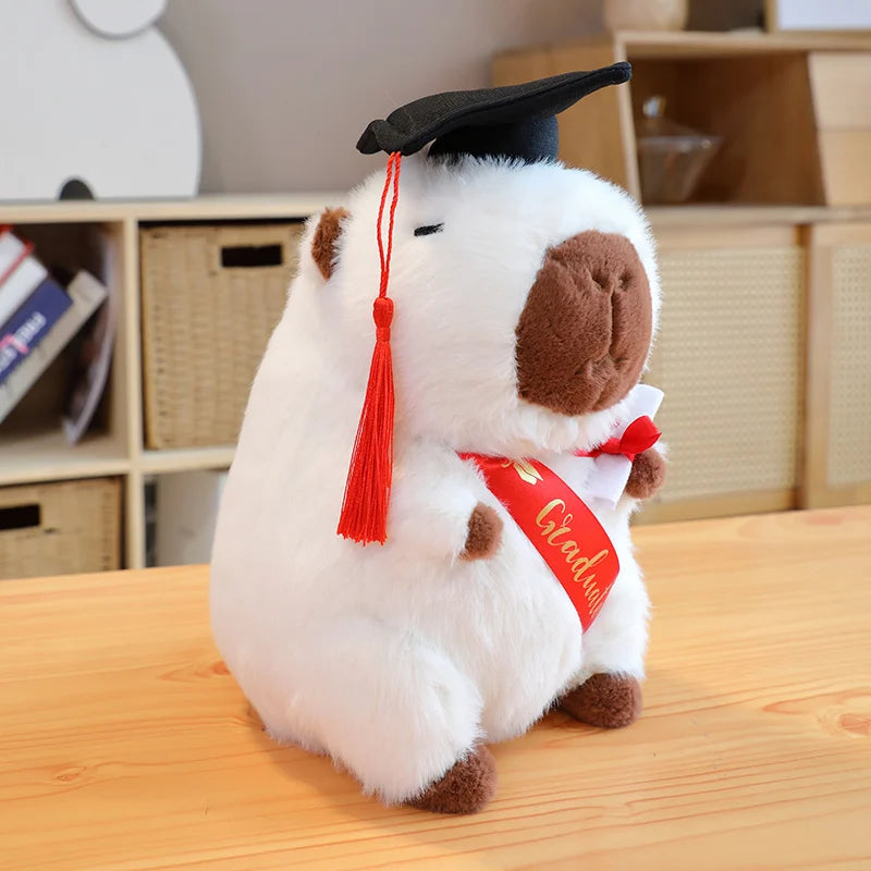 Capybara plush toy wearing a graduation cap and gown on a wooden surface