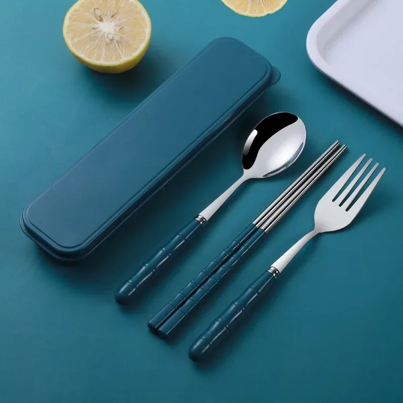 Set of silver kawaii utensils with blue handles on a teal surface, including a spoon, fork, and chopsticks.