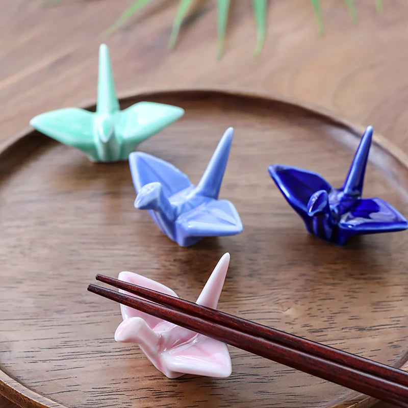 Four ceramic origami cranes kawaii chopstick holders in green, blue, and pink on a wooden surface with chopsticks.