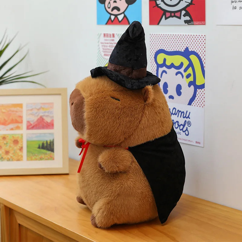 Capybara plush toy resembling a bear in a witch costume on a wooden surface with posters in the background.