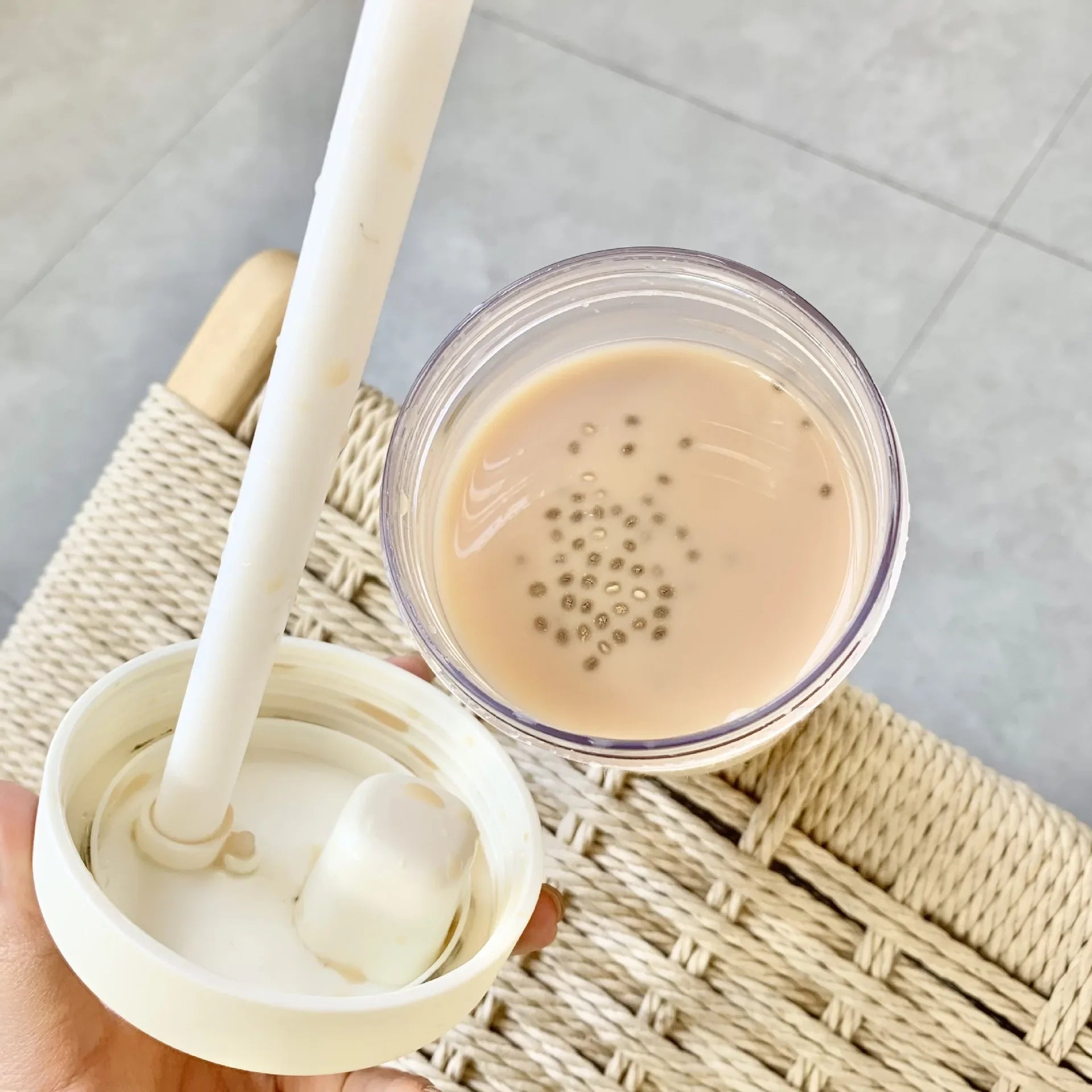 Hand holding a kawaii water bottle with a spoon, containing a beige liquid on a textured surface.