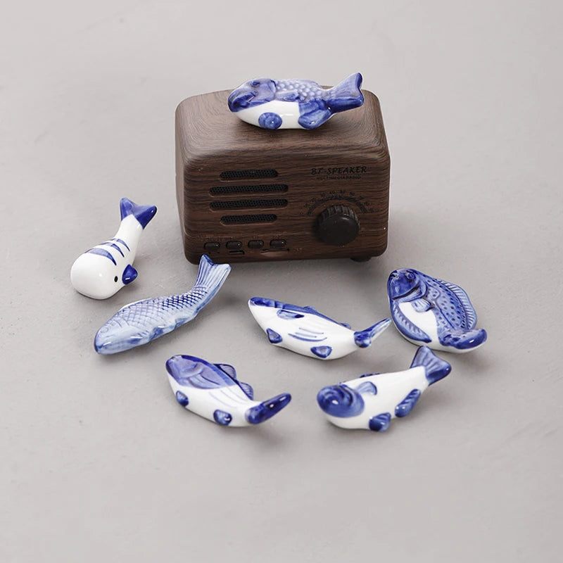 Set of blue and white ceramic fish-shaped kawaii chopstick holders with a wooden radio on a gray background