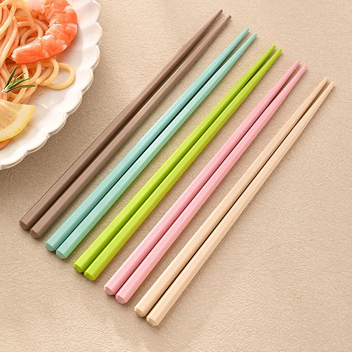 Set of colorful kawaii chopsticks on a beige surface with a plate of food in the corner.