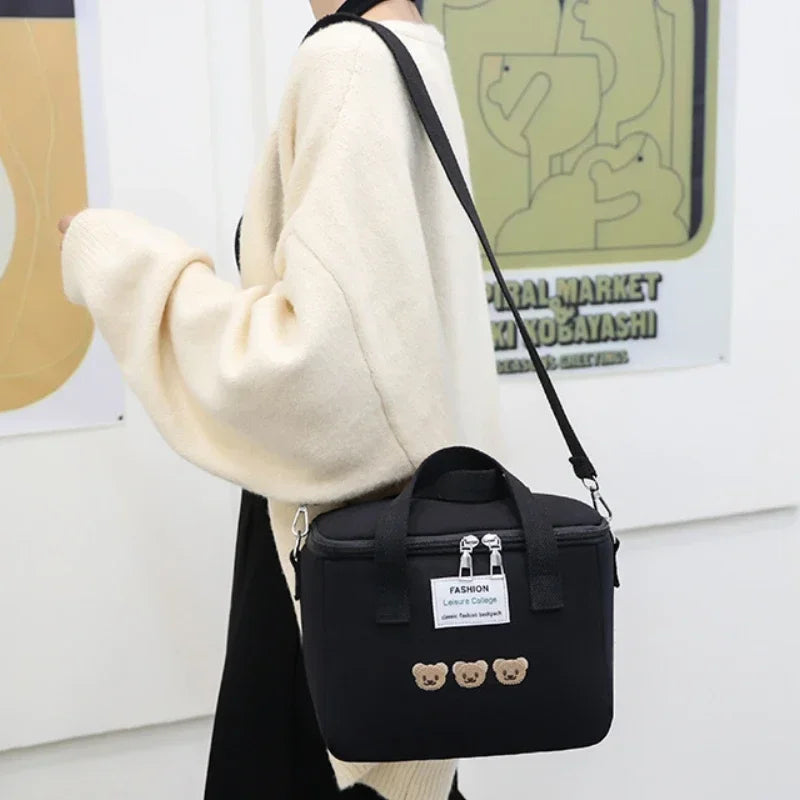 Black kawaii lunch bag with bear decorations worn by a person in a cream sweater