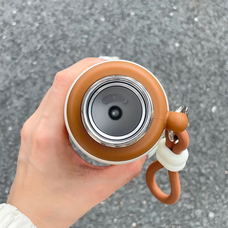 Hand holding a brown and white insulated kawaii mug with a gray background