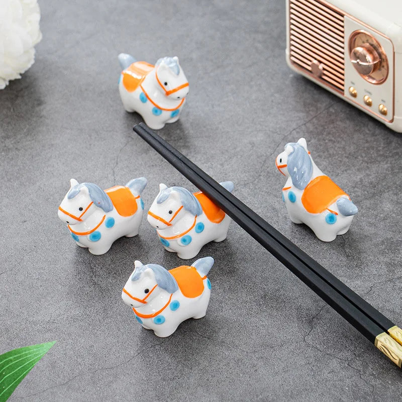 Set of four small horse-shaped kawaii chopstick rests on a gray surface with a vintage radio in the background.