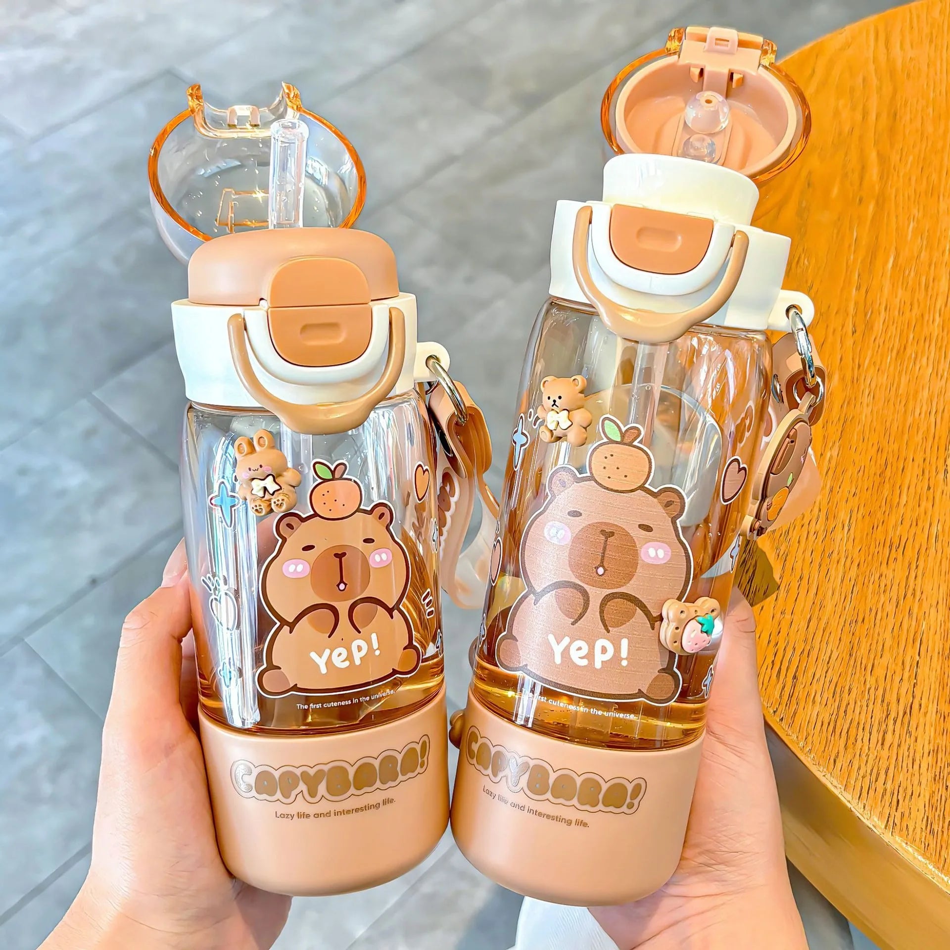 Two bear-themed kawaii water bottles held by a hand on a wooden surface.