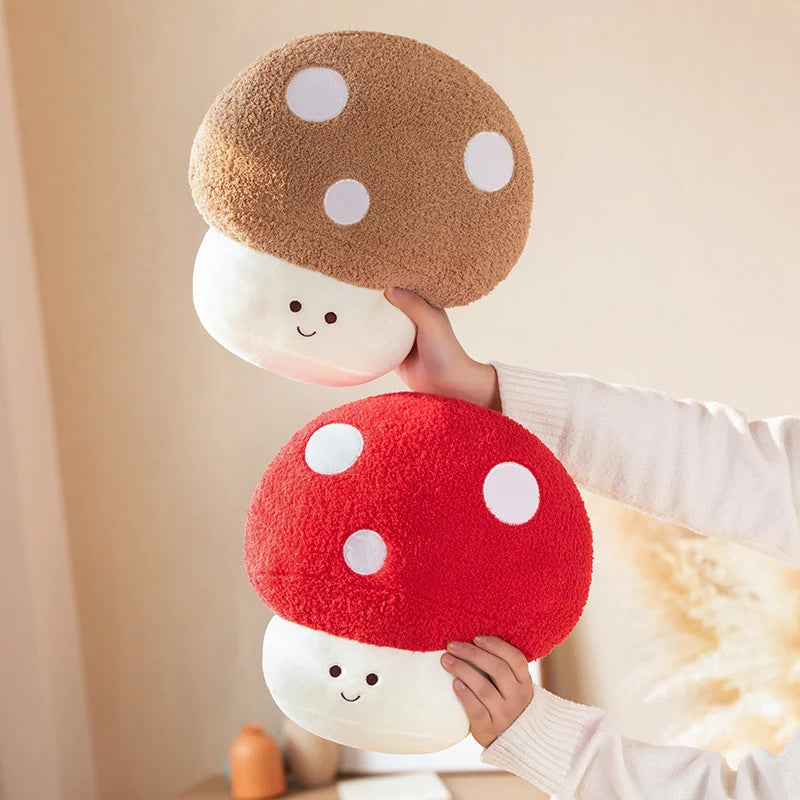 Person holding two kawaii plush mushroom toys, one red and one brown, against a neutral background.