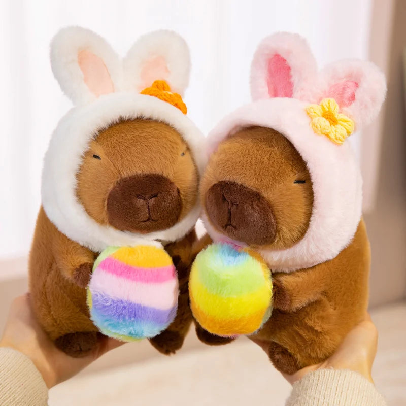 Two kawaii plush toys resembling bunnies with rainbow balls held by hands against a light background
