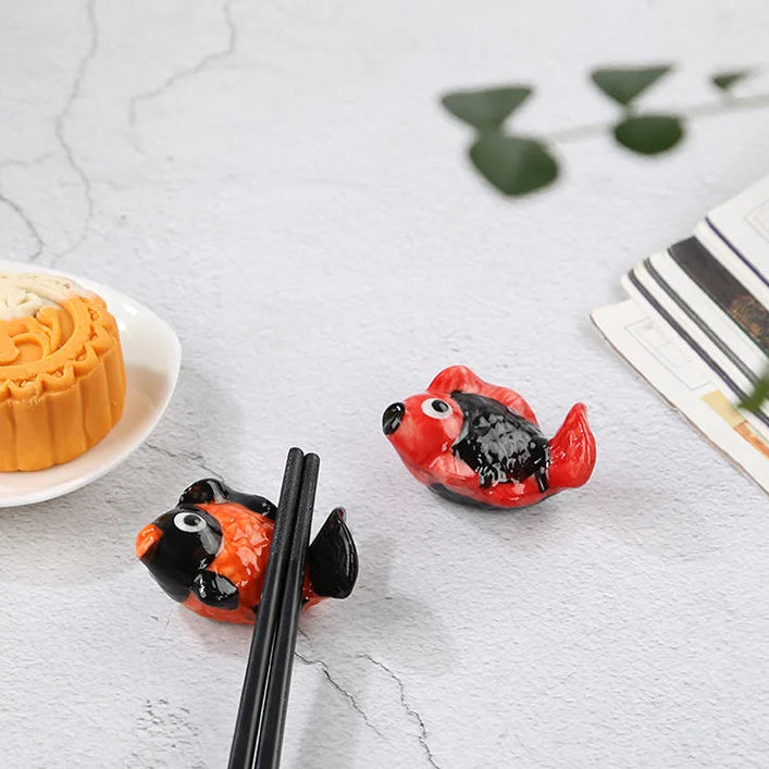 Fruit kawaii chopstick holders shaped like a fish on a marble surface with a plate of mooncakes.