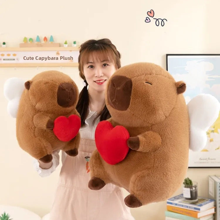 Person holding two large kawaii plush capybaras with red hearts, with a 'Cute Capybara Plush' sign in the background.
