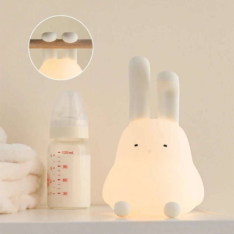 Rabbit-shaped kawaii night light next to a baby bottle on a neutral background