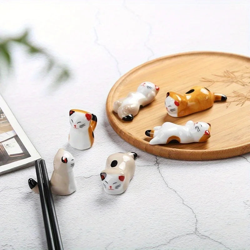 Set of small ceramic cat kawaii chopstick holder on a wooden plate with a blurred background