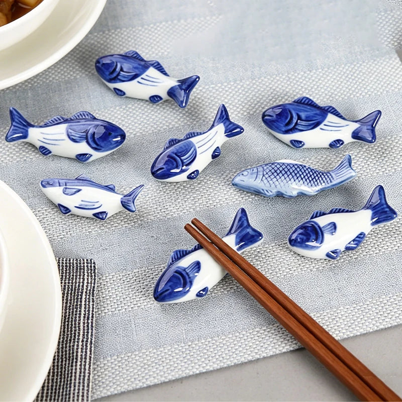 Blue and white ceramic fish-shaped kawaii chopstick holders on a gray surface with wooden chopsticks.